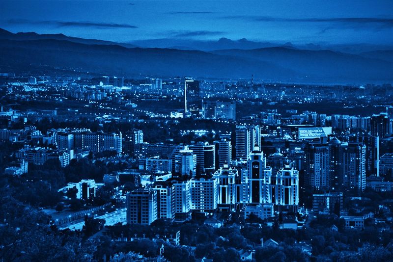 Вечерняя панорама Алматы с высоты: жилые и деловые кварталы, за ними горы Заилийского Алатау